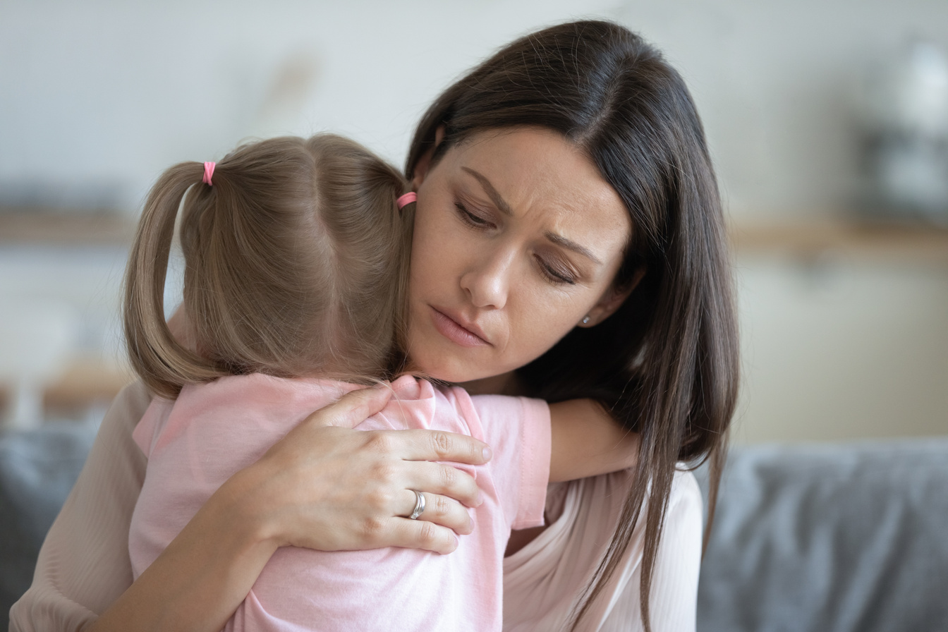 Worried young foster mother comforting embracing adopted child daughter